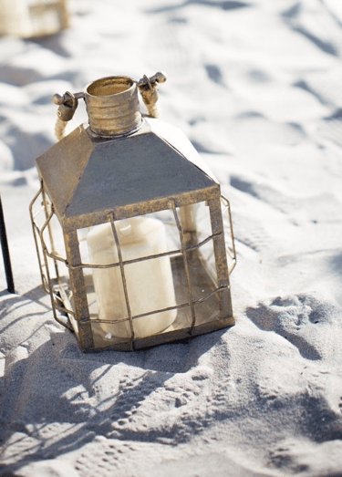 brass colored lantern with candle on the sand