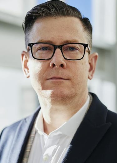 a man in a suit and glasses standing in front of a window
