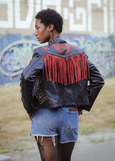 Fuller image of model looking over her shoulder, cool earrings and black denim jacket.