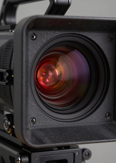 High-contrast close-up of a professional cinema camera sensor reflecting a studio setup. Deep black textures and dark charcoal grey metallic finishes. A single vibrant crimson red tally light is illuminated.