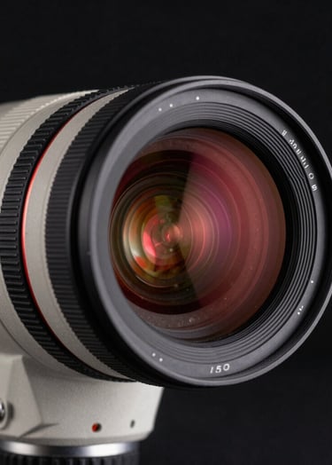 A close-up photograph of a professional cinema lens reflecting a faint vivid deep red glow. The background is a deep black studio, creating a mysterious and technical atmosphere. Soft off-white light catches the metallic edges of the camera gear.