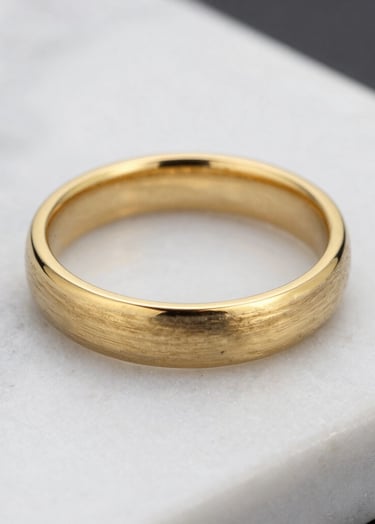 A detail shot of a brushed gold wedding ring set against a textured white marble surface. Sharp focus, high-end luxury feel, North American / US context.