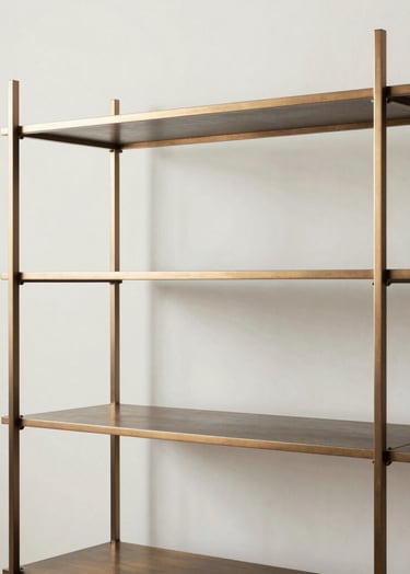 A minimalist shelving unit crafted from hand-polished warm bronze and dark steel. The piece stands against a soft off-white wall in a bright studio setting. Sharp lines and clean geometric intersections are highlighted by natural daylight.
