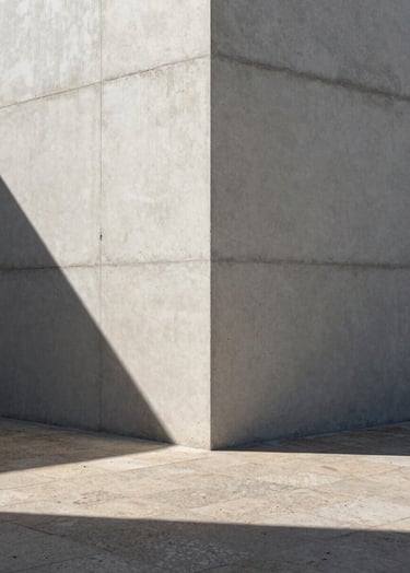 Detailed architectural photography of a raw concrete wall corner meeting a textured stone floor, sharp dramatic shadows from direct sunlight, minimalist European Portuguese architecture style, off-white and slate grey tones.