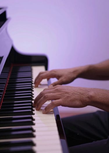 An action shot of hands playing a piano under a pale lavender spotlight. The aesthetic is moody and soulful, reflecting a live musical performance. Professional lighting, sharp detail on the keys.