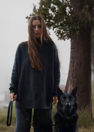 A woman in an oversized sweater stands with her black dog pet photography in Wakefield
