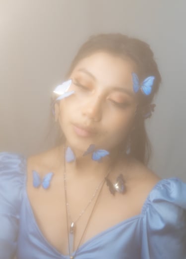 Same self portrait as home page, hazy dreamy with blue butterflies on face and neck.