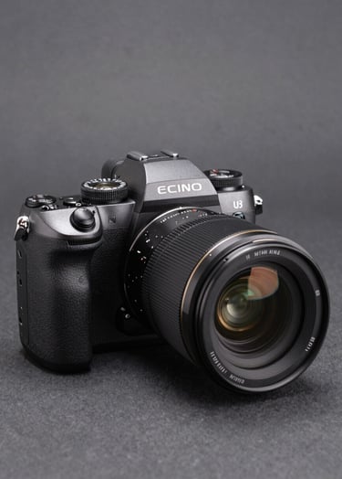 A sleek professional mirrorless camera with a large lens, positioned on a minimalist charcoal gray background, sophisticated studio lighting creating soft highlights on the metallic body, professional product photography, North American / US style.