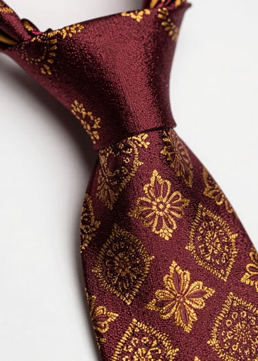 Macro shot of a silk jacquard tie knot in deep burgundy and gold patterns, rich texture under warm focused studio light.