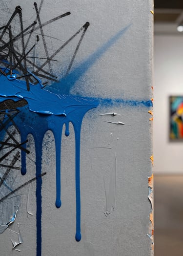 A detailed close-up of a contemporary mixed-media canvas. The surface shows thick layers of light grey acrylic paint, vibrant blue spray paint drips, and charcoal scribbles. The lighting is crisp and editorial, highlighting the heavy texture of the paint, set in a International / Urban Art Scene gallery environment.
