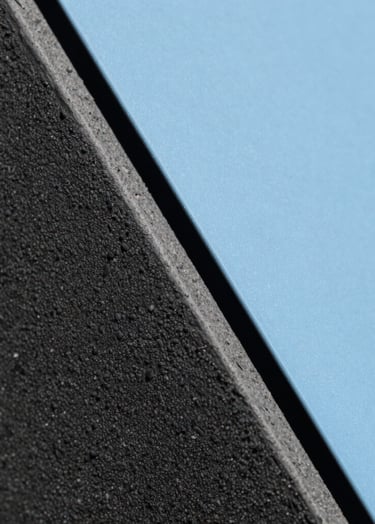 Macro photography of textured dark grey materials and a smooth baby blue surface meeting at a sharp diagonal line. The lighting creates a high-contrast, professional, and abstract look. South American architectural detail style.