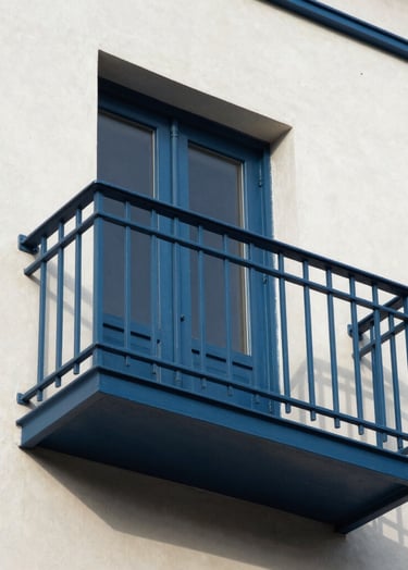A refined architectural detail of a Steel Blue balcony against a crisp Off-White building wall, captured in sharp, natural daylight.