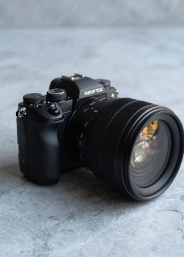 A professional high-end camera lens resting on a mist grey marble surface. Minimalist composition with slate blue shadows and a soft, sophisticated light source.