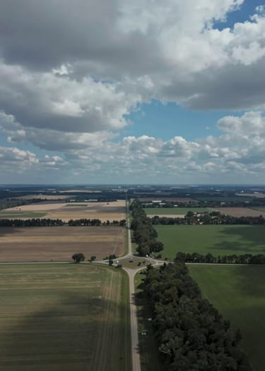An aerial documentary-style photograph of a rural landscape under a dramatic sky, showing the intersection of nature and infrastructure. High contrast and professional grade, reflecting clear communication. Uses colors #263238 and #B0BEC5.