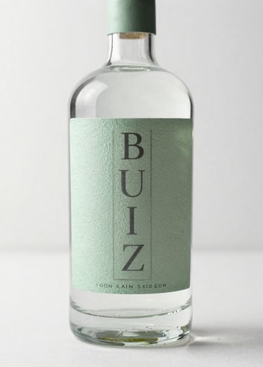 A high-end professional photograph of a premium gin bottle with a textured soft sage green label and charcoal typography. The bottle is placed on a minimalist mist white surface in a bright North American / US design studio, with soft natural light highlighting the glass texture.