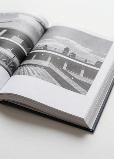 Photography of an open art book on a clean white surface. The pages show black and white architectural photography. The lighting is bright and even, highlighting the paper texture and the minimalist layout.