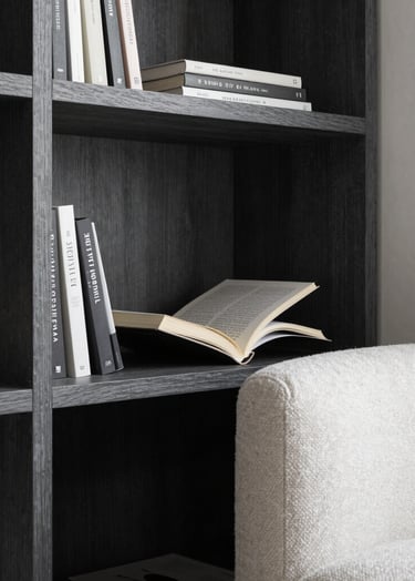 A close-up of a designer reading nook in a South American apartment, featuring a charcoal wood bookshelf and a comfortable off-white textile armchair, elegant soft lighting, professional photography.
