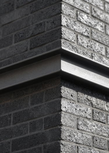 An 'action' shot of a finished architectural detail. A sharp corner of a brick wall meeting a metal beam. Cinematic side lighting creating strong contrast. Touches of #6B705C in the shadows. Editorial style, sharp and clean.