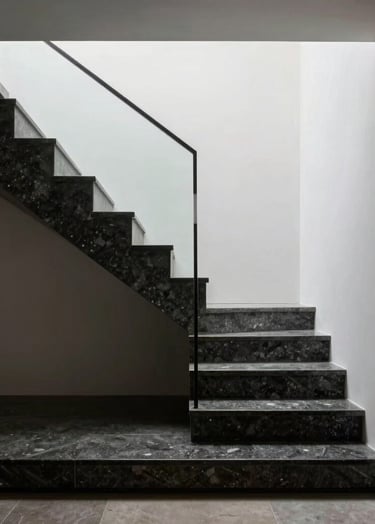 A minimalist architectural staircase inside a luxury home in Brazil. The steps are made of dark basalt stone against a white wall. Dramatic top-down lighting creating high contrast. Editorial architectural style.