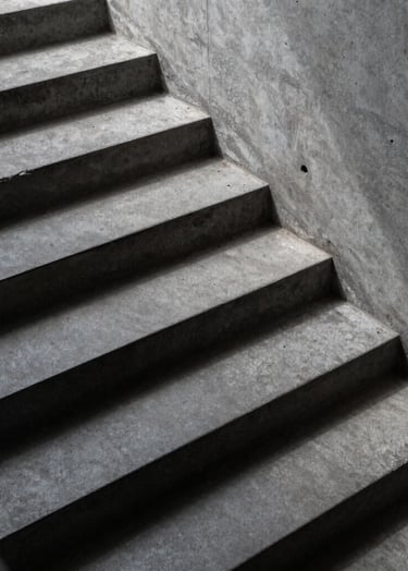 High-angle shot of a minimalist concrete staircase with sharp midnight slate shadows and dusty steel grey surfaces.
