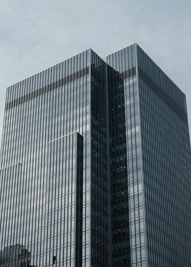 A minimalist architectural detail of a glass and steel skyscraper in a North American / US city, sharp geometric angles against a soft gray sky, high contrast lighting, cool blue-gray tones.