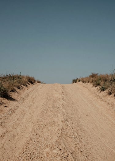 A low-angle shot of a dusty clay-colored trail leading into the horizon under a muted steel blue sky, wide-angle lens, natural lighting.