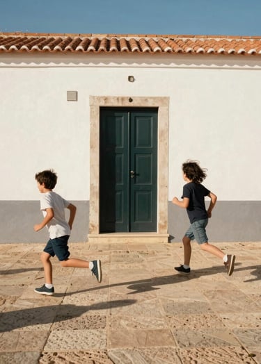 Spontaneous shot of children running across a sun-bleached patio in a European Portuguese coastal village. The background features white-washed walls and a deep charcoal door. Vivid, warm light and joyful atmosphere.