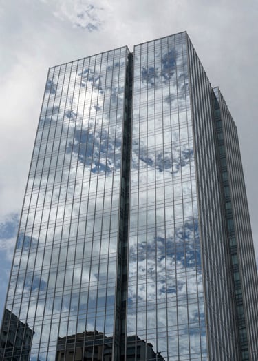 Architectural detail of a modern glass skyscraper in São Paulo, Brazil. The building reflects a cloud white and soft blue grey sky. The shot is taken from a low angle looking up, symbolizing growth and professional forward-thinking.