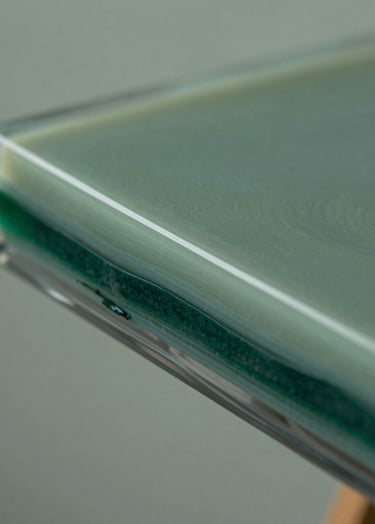A close-up side profile shot of the resin painting, emphasizing the thickness of the translucent layers. The depth of the muted sage green and deep forest green pigments is visible through the clear, polished resin edge.