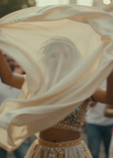 A dynamic shot capturing motion blur of fabric or movement during a celebration. It feels alive and authentic. The lighting is warm and golden, utilizing #C4B29A and #6F604F to maintain a premium, artistic aesthetic.