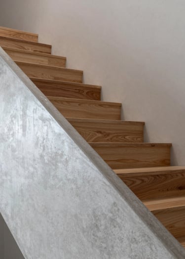 Detail of an interior staircase combining concrete and wood. Neutral palette of light silver gray and warm timber. Sophisticated composition with sharp focus on the materials.