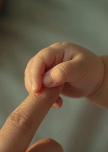 A detailed shot of a baby's hand grasping a mother's finger. Cinematic lighting with warm, golden highlights. The background is a soft, blurred #F8F0E3 fabric. Intimate and authentic lifestyle photography.