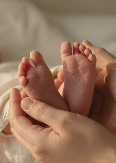 A cinematic close-up of a newborn's tiny feet resting in a parent's hands. The lighting is soft and golden, suggesting a sun-drenched afternoon. The textures of a #F8F0E3 linen blanket are visible. The mood is intimate, authentic, and filled with warmth.