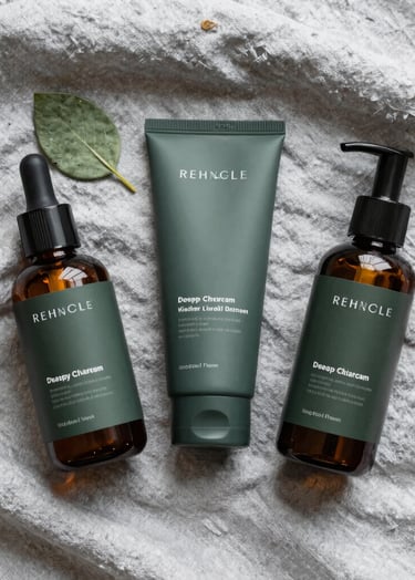 A flat lay of skincare essentials on a Soft Silver Mist linen cloth. A single green leaf adds a touch of Muted Sage, while the Deep Charcoal Green product labels provide a sharp, modern contrast.