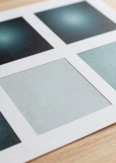 Fine art photography of printed research documents and design swatches laid out on a light wood surface. The lighting is soft and professional, highlighting the quality of the Pale Frost paper and Muted Teal ink.