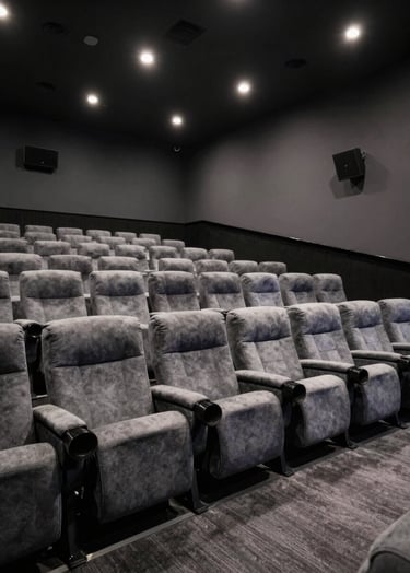 A wide-angle photograph of a sophisticated North American cinema screening room with plush slate grey seating and soft spotlighting. The atmosphere is professional and cinematic, reflecting high-end film distribution standards.