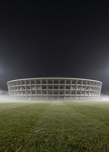 A wide, atmospheric shot of an empty arena at night, soft fog rolling over the grass, charcoal sky, minimalist and premium editorial mood.