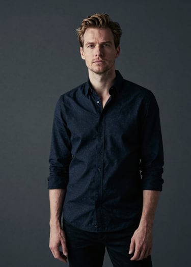 Full-bleed editorial portrait of a Northern European / Dutch creative professional in a charcoal-toned minimalist space. Premium lighting, sophisticated and understated mood, using a dark color palette with off-white highlights.