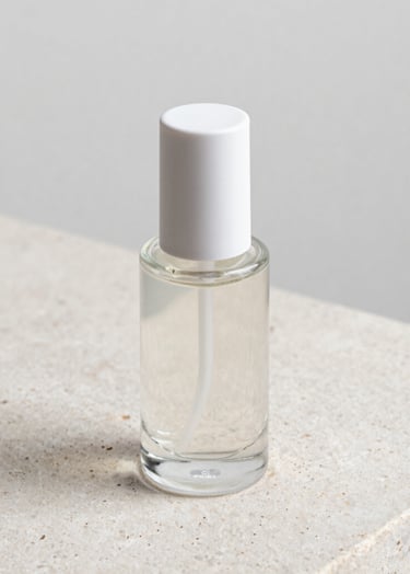 Close-up of a premium glass cosmetic bottle resting on a textured light stone surface. The lighting is precise, highlighting the glass edges and fluid contents. Minimalist composition with extreme focus on quality and clarity. Palette: #F8F5F2, #8E8E8E.