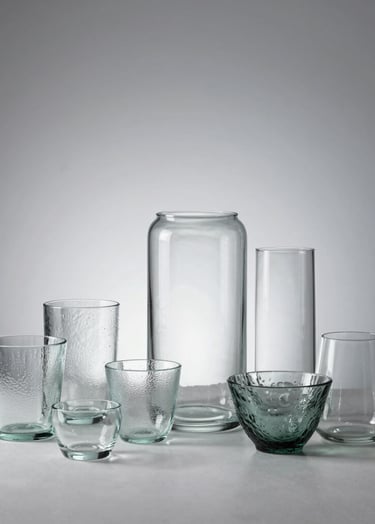 A minimalist studio setup with various textured glass objects, captured in soft natural light against a pale silver background, reflecting a professional photography studio in Central Europe.