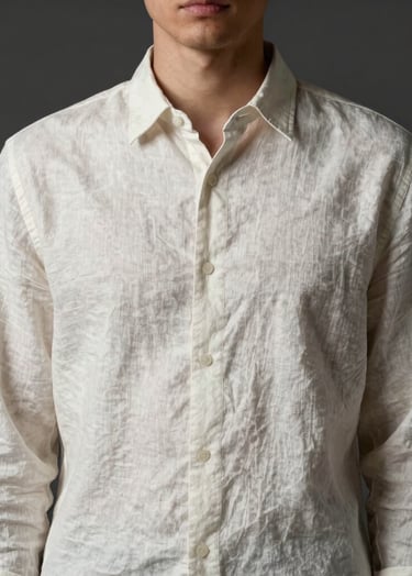 A high-fashion portrait of a person in a minimalist off-white linen shirt, posed against a dark charcoal background. The composition is focused on the upper body, with soft side lighting that accentuates the fabric texture in a Northern European studio setting.