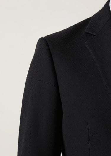 Close-up detail of a high-end black garment showing intricate stitching and premium texture. The lighting highlights the craftsmanship against an off-white #F8F8F8 background. Artistic and refined.