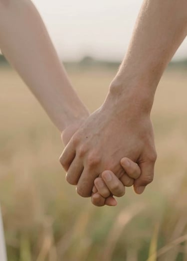 Macro shot of two people holding hands in a field, intimate and emotive. Soft focus background, warm #F8F4F0 skin tones and soft golden hour light.