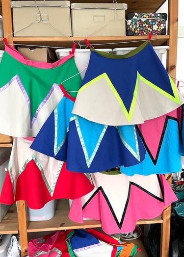 Handmade colorful circus skirts with zigzag patterns hanging on a wooden storage rack.