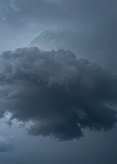 A minimalist macro photograph of a heavy storm cloud, showcasing textures of deep charcoal and steel blue, dramatic side-lighting highlighting the vapor, clean and atmospheric composition, International / Western style.
