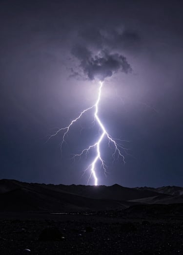 A powerful lightning strike over a dark charcoal mountain range, a brilliant flash of blue-white light against a deep navy grey sky, minimalist aesthetic with high contrast, International / Western landscape.