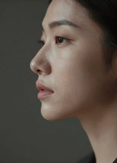 A sophisticated fine art portrait of a person's profile. Light highlights the bridge of the nose and the chin, while the rest of the head fades into the dark background #1F1E1C. Elegant and emotive, capturing authentic human expression. Warm, personal lighting #F5F2EF.