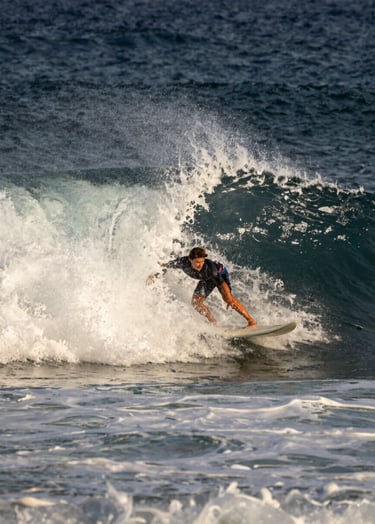 A professional surfer navigating a powerful barrel wave, Western / International coastal setting, high contrast lighting, spray of water caught in mid-air, dark midnight blue ocean and off-white sea foam.