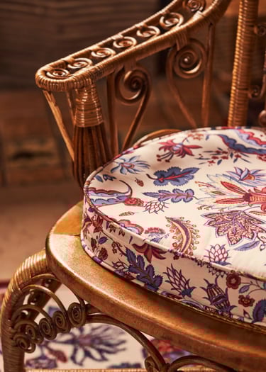 Fauteuil en osier avec posé dessus un coussin recouvert d'un tissu à motifs floraux