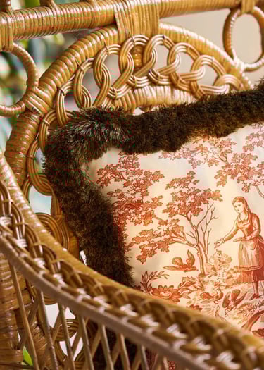 Fauteuil en osier avec posé dessus un coussin de toile de jouy et marabout rasé sur le tour